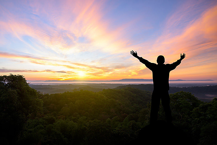 Silhouette of man raised hands with landscape mountains at sunset